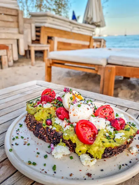 Avokado ve krem peynirli, böğürtlen ve çiçekle süslenmiş ve plajda servis edilmiş
