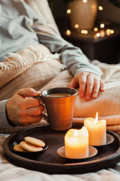 a caucasian man relaxing at home, lighting candle, drinking coffee in bed under blanket