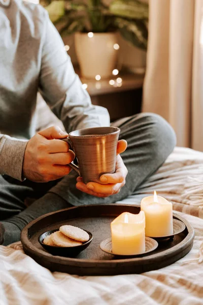a caucasian man relaxing at home, lighting candle, drinking coffee in bed