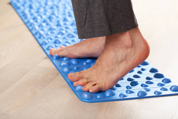man doing flatfoot correction gymnastic exercise walking on massage mat at home