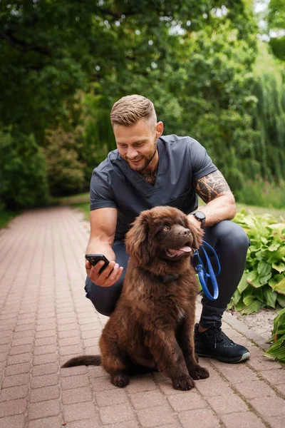 带着狗在公园里散步和在公园里用手机的快乐男人的画像 — 图库照片