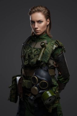 Kahverengi saçlı, gaz maskeli, kamuflaj kostümü giymiş asker bir kadın..