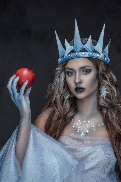 Портрет привлекательной ледяной королевы с красным яблоком и замерзшей кожей, смотрящей в камеру.