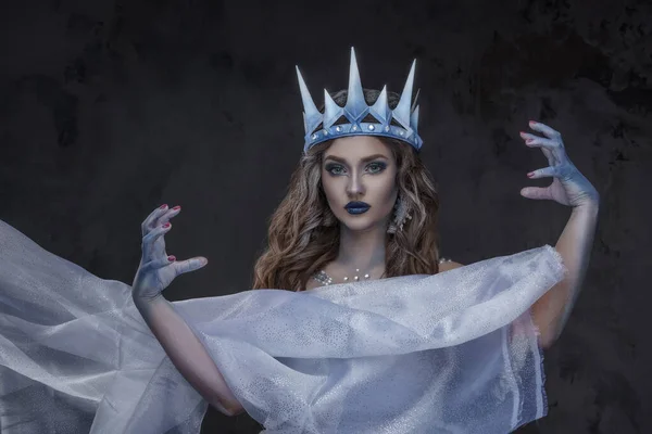 Studio shot of ice princess dressed in cloak and crown against dark background.