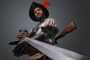 Gri ortaçağ silahşöründen izole edilmiş kameraya bakıyor ve kılıcı kameraya doğrultuyor..