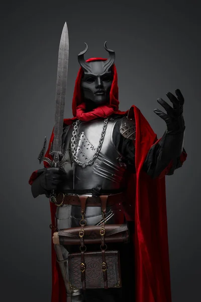 Portrait of member of dark cult dressed in black mask and red robe holding sword.