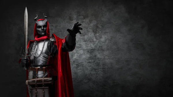 Shot of leader of esoteric cult dressed in silver armor and red mantle with horned mask.