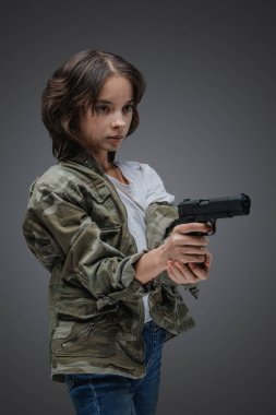 Shot of bold young girl with camouflage jacket and handgun against gray background.
