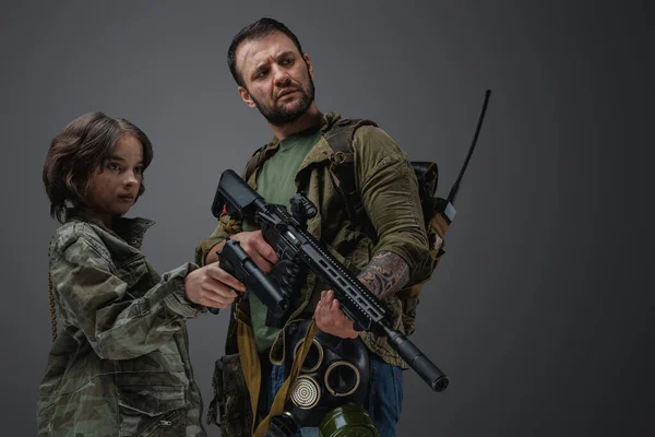 Studio shot of post apocalyptic military man protecting young girl against gray background.