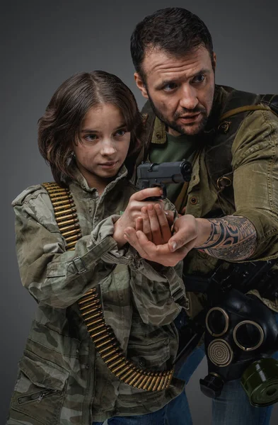 Portrait of post apocalyptic man teaching little girl to shoot in setting of post apocalypse.