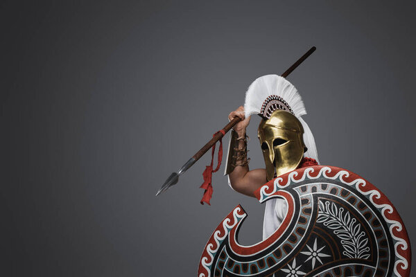 Studio of furious spearman from ancient greece dressed in armor and cloak.