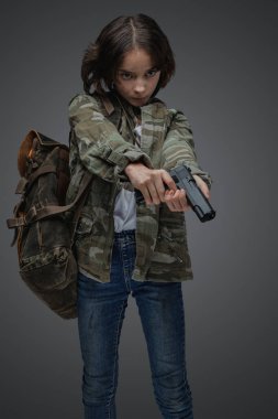 Portrait of little girl survivor with camouflage clothes holding handgun in setting of post apocalypse.