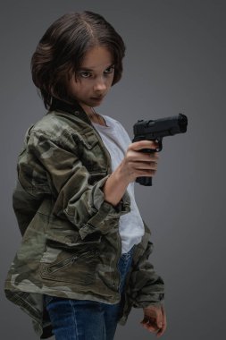 Shot of bold young girl with camouflage jacket and handgun against gray background.
