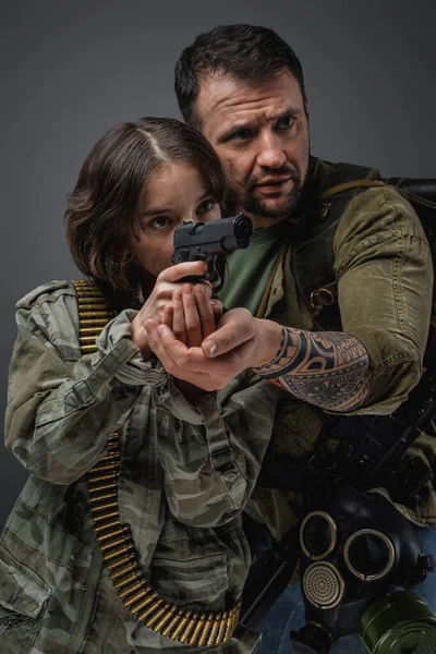 Portrait of post apocalyptic man teaching little girl to shoot in setting of post apocalypse.