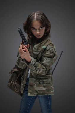 Portrait of little girl survivor with camouflage clothes holding handgun in setting of post apocalypse.