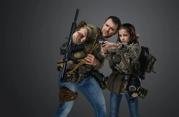 Portrait of man training little girl to shoot handgun in setting of post apocalypse.