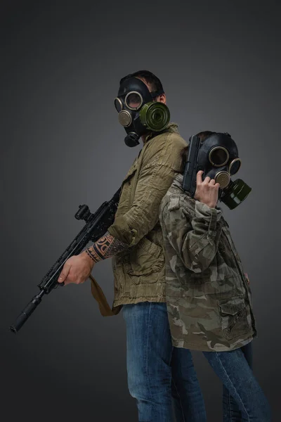 Shot of adult man and young girl in post apocalyptic style with gas masks and guns.