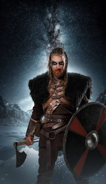 Portrait of ancient viking with shield and axe staring at camera against stars.