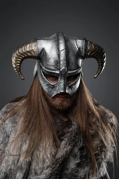 Studio shot of fierce nordic warrior with long hairs dressed in fur and horned helmet.