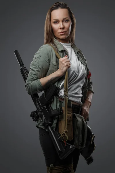 Portrait of killer woman with rifle in post apocalyptic style against gray background.