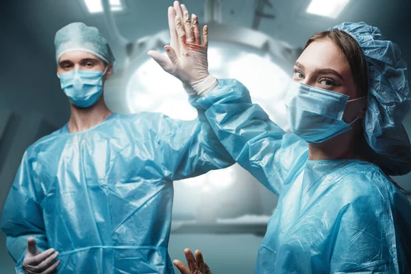 Shot of two doctors with masks and robes looking at camera in operating room.
