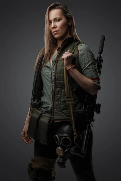 Portrait of military woman with rifle in post apocalyptic setting against grey background.