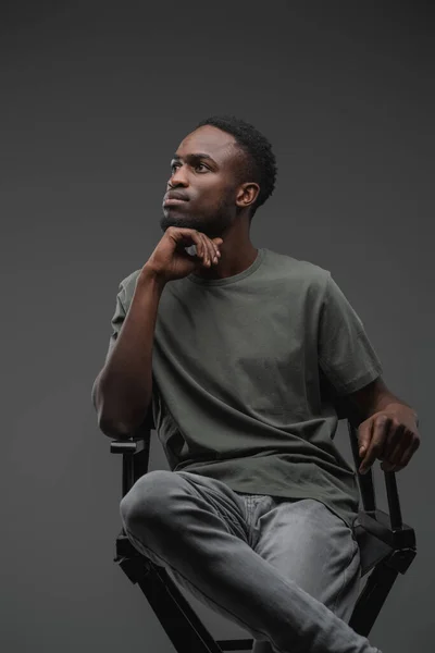 スタジオショットの思考アフリカ人男性のカジュアルな服装で座って椅子に座って — ストック写真