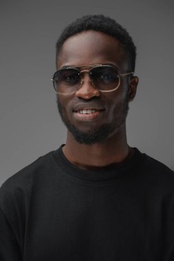 Afrika kökenli gülümseyen bir adamın son moda güneş gözlüğü ve günlük kıyafet giydiği bir fotoğraf..