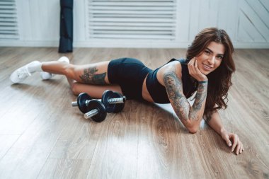 Siyah spor ayakkabılı, dövmeli, spor ayakkabılı kız dairenin dambıllarının etrafında poz veriyor..