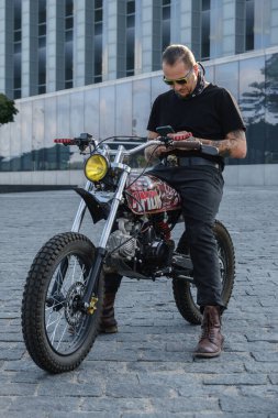 Motosikletli bir sürücünün portresi. Siyah kıyafetler ve akıllı telefon..
