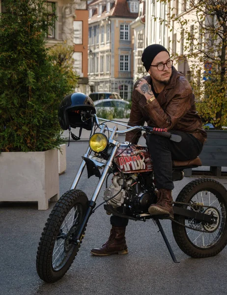Homme Beau Biker Rider En Veste De Cuir Noir Et Jeans Mis Casque Près De La  Moto De Style Classique Café Racer. Vélo Fait Sur Mesure Dans Le Garage  Vintage. Style De