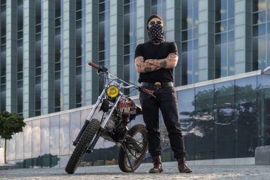 Bandanalı ve motosikletli kolları çapraz pozlu dövmeli şehir bisikletçisinin portresi..