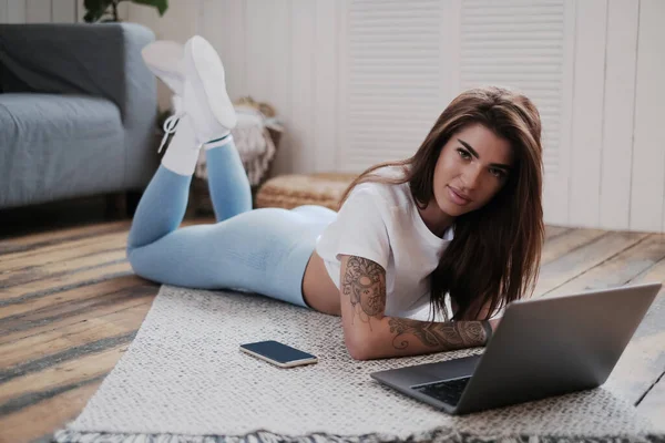 Ung Och Tatuerad Flicka Tittar Kameran Liggande Golvet Med Laptop — Stockfoto