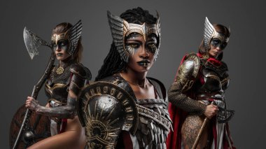 Gri arka planda makyajlı ve zırhlı üç Amazon stüdyo fotoğrafı..