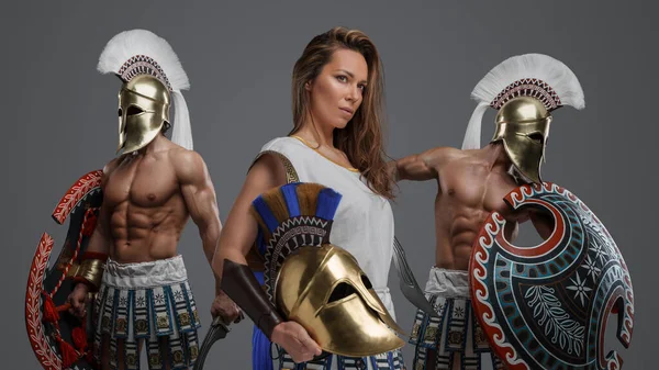 Studio shot of warrior woman and two muscular swordsmen from ancient greece.