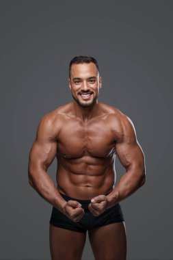 Keskin vücutlu nefes kesen yakışıklı erkek model, gri arka planda siyah bir külot giyip, karizma ve seksapel çekiciliğine karşı etkileyici bir gülümseme sergiliyor.
