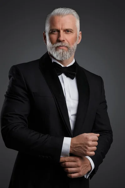 有魅力的中年男子 头发灰白 胡须灰白 身穿时髦的黑色西服 打着领带 在拍摄灰色背景的照片时 他扮演了一位温和的特工 — 图库照片