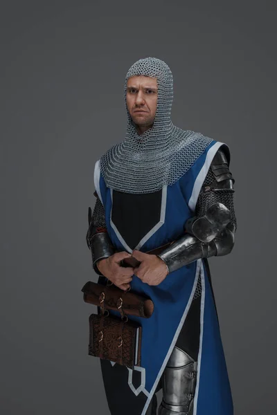 中世の武士の鎧 青のコート チェーンメールフード輝く剣をつかんで 断固として中立的な灰色の背景に立って — ストック写真