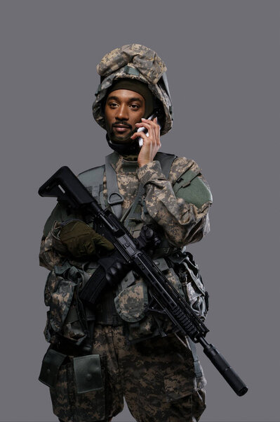 A young military man in uniform and helmet talks on the phone with a smile, displaying the communication skills of soldiers in uniform