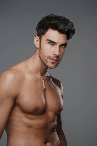 Charismatic close-up of a shirtless brunette model with a fit and toned physique against a modern gray backdrop