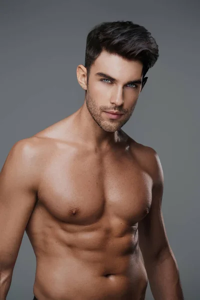 Charismatic close-up of a shirtless brunette model with a fit and toned physique against a modern gray backdrop