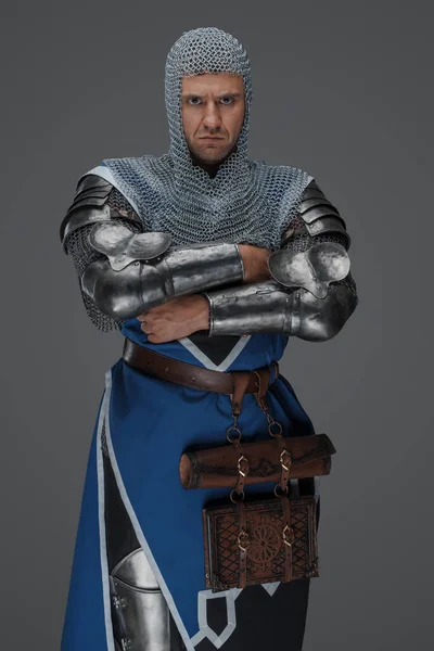 中世の鎧と青のコートを身に着けている勇敢な王室の警備員 チェーンメールのコイフと 腕を組んで立って 灰色の背景を背景に — ストック写真