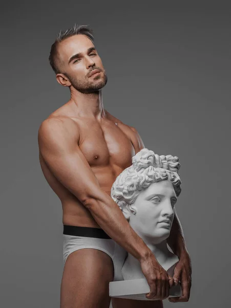 彼の体に対して押された古代ギリシャのバスト彫刻とポーズをとって 灰色の背景を背景に設定 — ストック写真