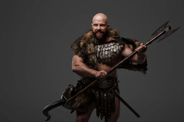An angry and yelling bearded Viking warrior wearing fur and lightweight armor against a gray backdrop