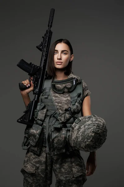 スタジオの肖像画にエレガントにポーズをとるグレーの背景に対して自動ライフルを保持する軍服を着た素晴らしい女性兵士 — ストック写真