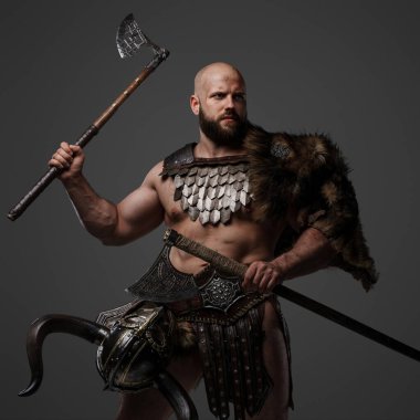 Sert, kaslı, sakallı, kürk ve hafif zırh giymiş, beline bir kask takmış gri bir arka plana karşı iki balta sallayan bir Viking savaşçısı.