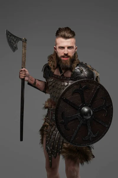 Fierce bearded Viking dressed in fur and light armor wielding an axe against a gray background