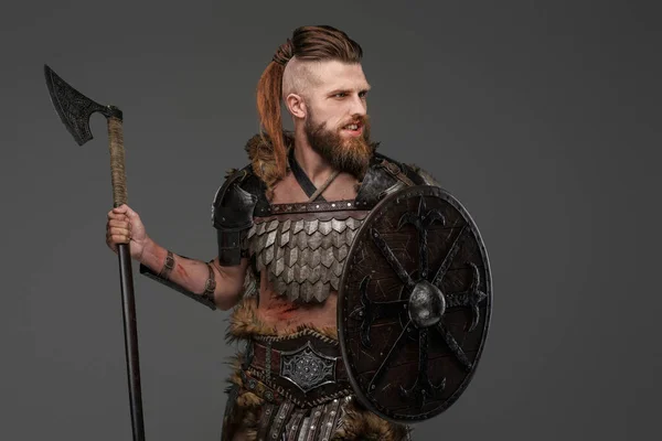 Fierce bearded Viking dressed in fur and light armor wielding an axe against a gray background