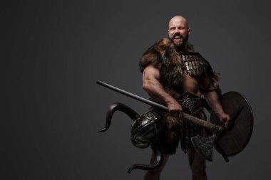 Kızgın ve bağıran sakallı bir Viking savaşçısı. Kürk ve hafif zırh giymiş gri bir arka plana karşı.