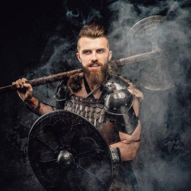 Kürk ve hafif zırhlı sakallı bir Viking 'in çarpıcı bir görüntüsü. Güçlü bir balta ve kalkan taşıyor.